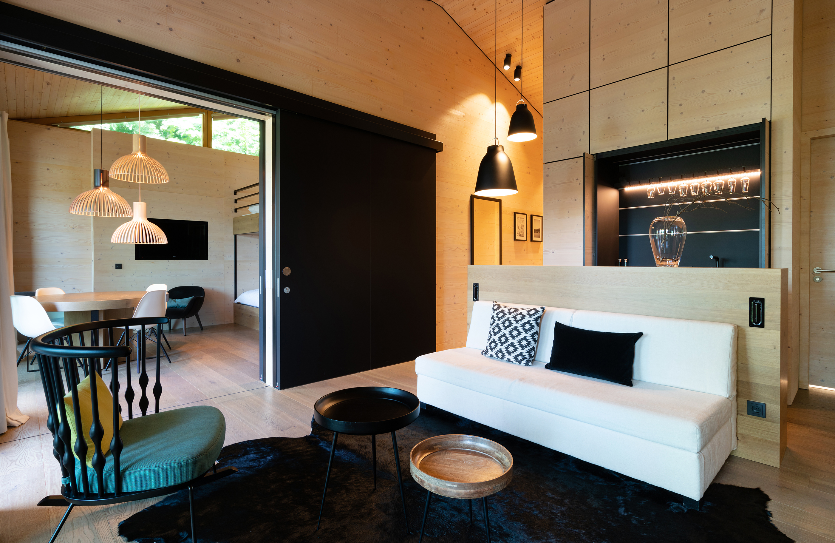 Aufnahme im Wohnbereich des Alpenchalets mit einem weißen Sofa und Blick in das angrenzende Zimmer mit Stockbetten