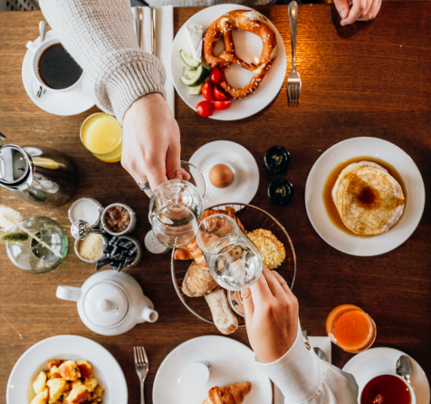 Üppig gedeckter Frühstückstisch mit zwei Personen, die mit einem Sektglas anstoßen