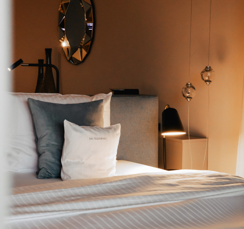 Einblick in ein Zimmer mit frisch gedecktem Bett und blauen Kissen