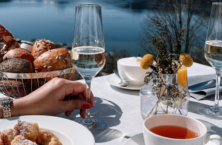 Gedeckter Brunch Tisch mit Sektglas in der Hand und Panoramablick über den Tegernsee